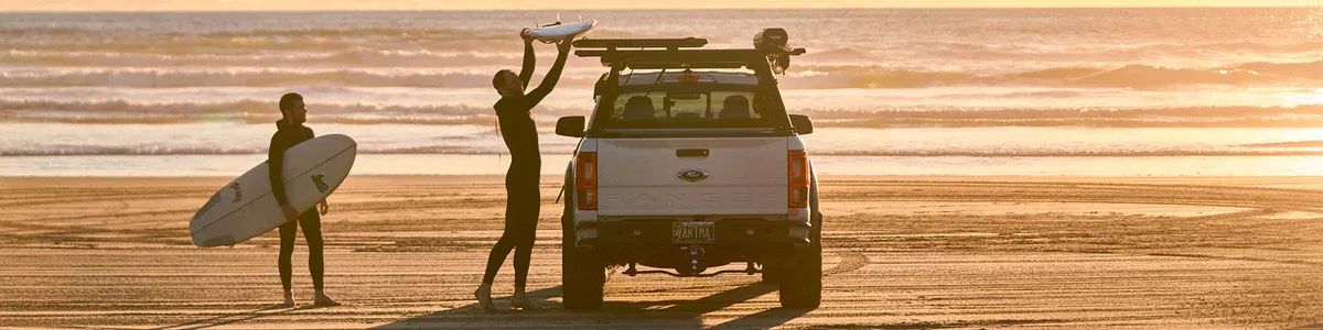 A lakeshore scene featuring a couple loading paddleboards on their car.