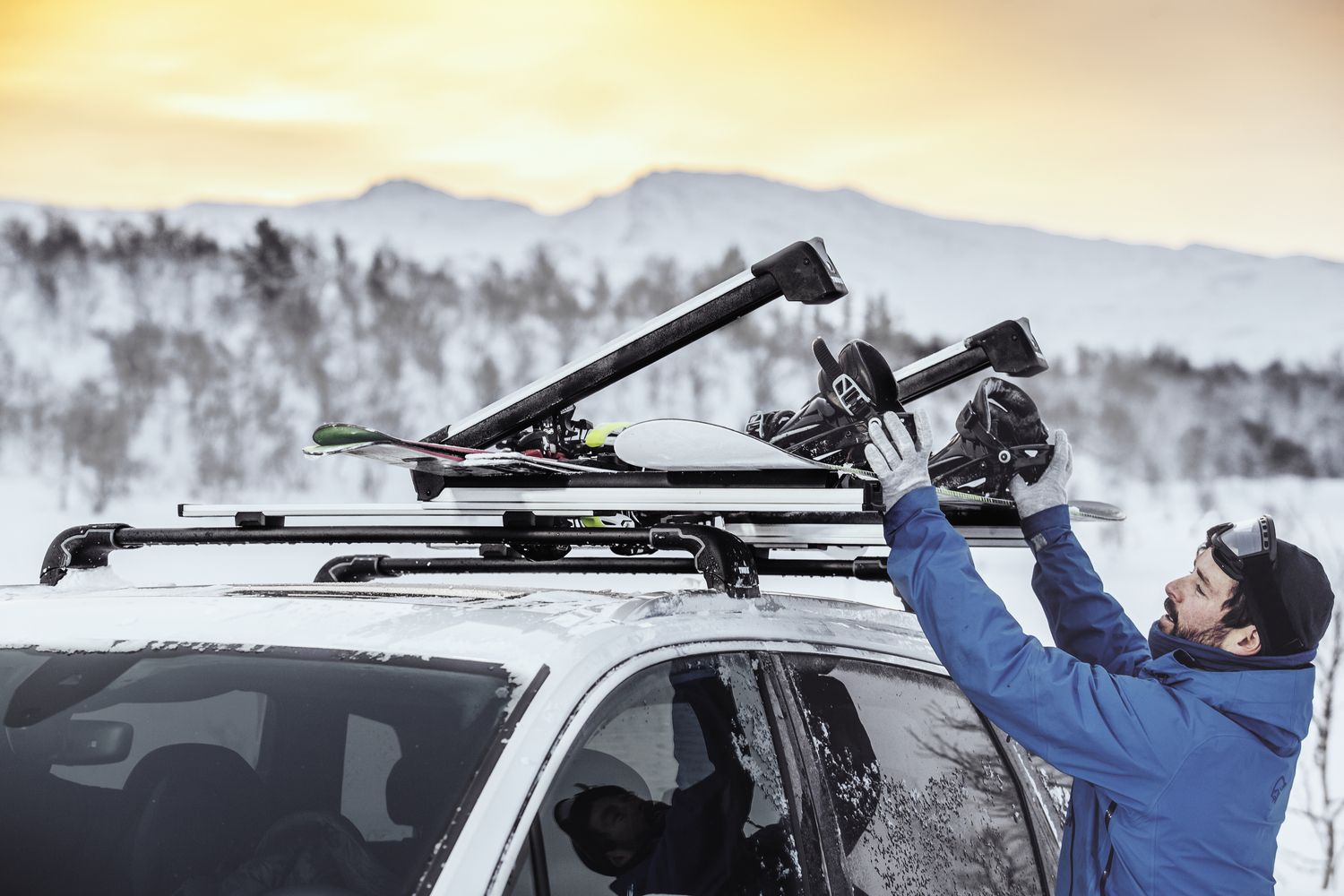 skis and snowboards being loaded into a roof mounted ski carrier